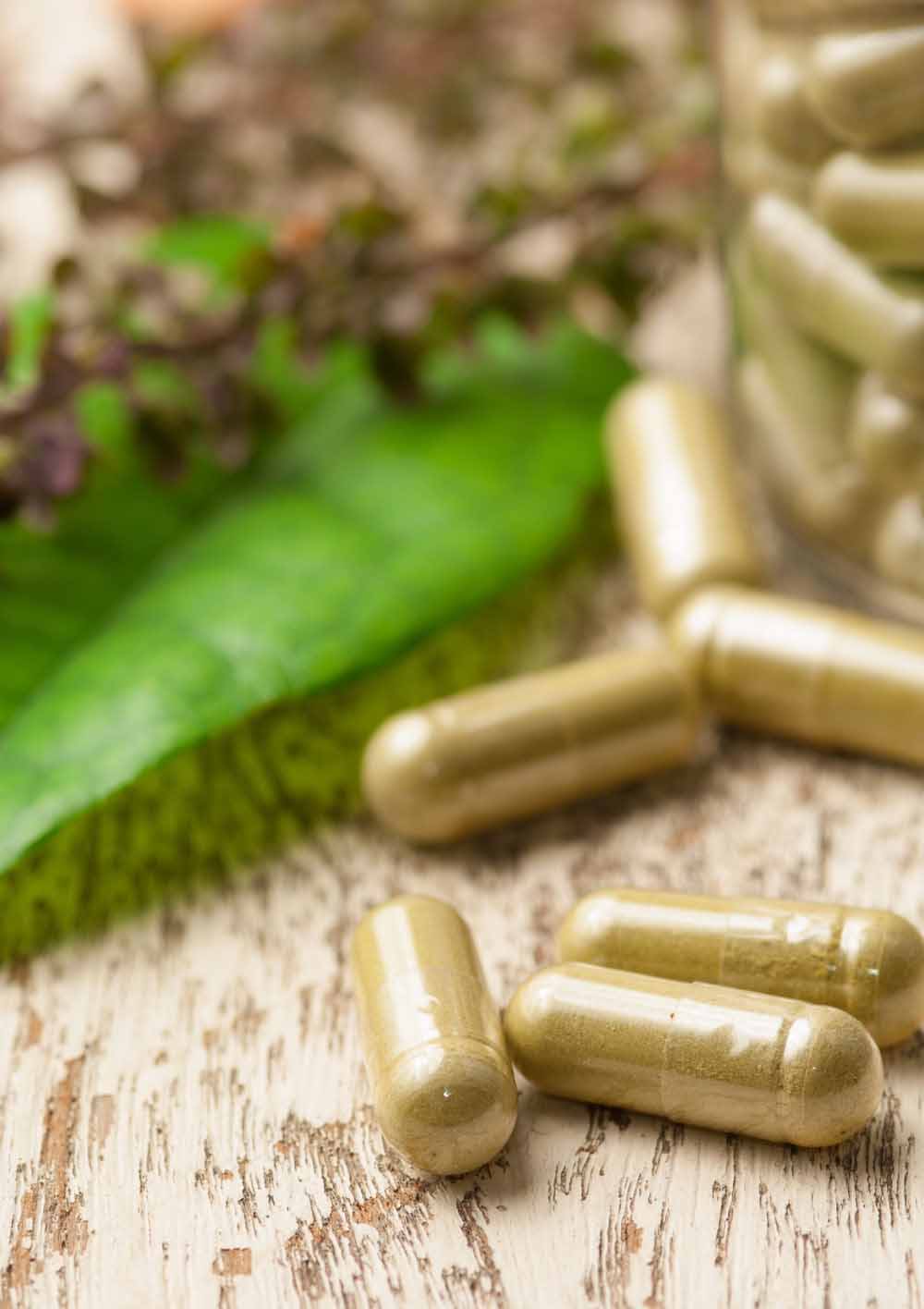 Herb capsule with green herbal leaf on wood